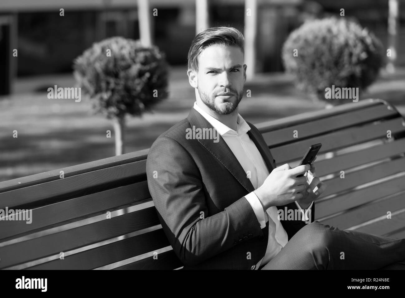 Man verwendet werden Smartphone im Park. Manager mit Handy an sonnigen Außenpool. Unternehmer im blauen Anzug sitzen auf der Bank. Das moderne Leben und Business Lifestyle. Business Kommunikation, neue Technologie und sms. Stockfoto