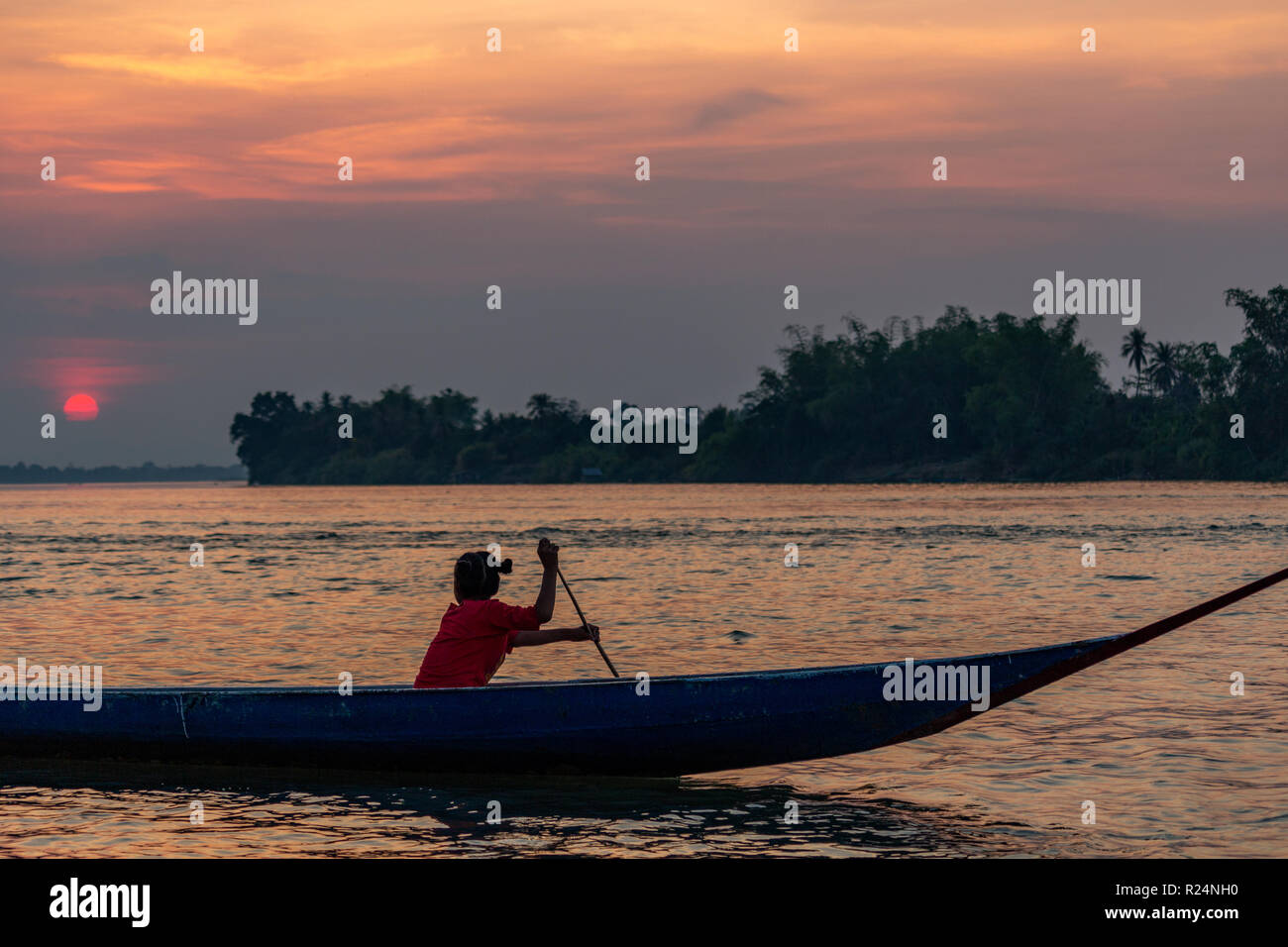 Don Det, Laos - April 22, 2018: Mädchen Rudern ein hölzernes Boot über den Fluss Mekong bei Sonnenuntergang in der Nähe der kambodschanischen Grenze Stockfoto