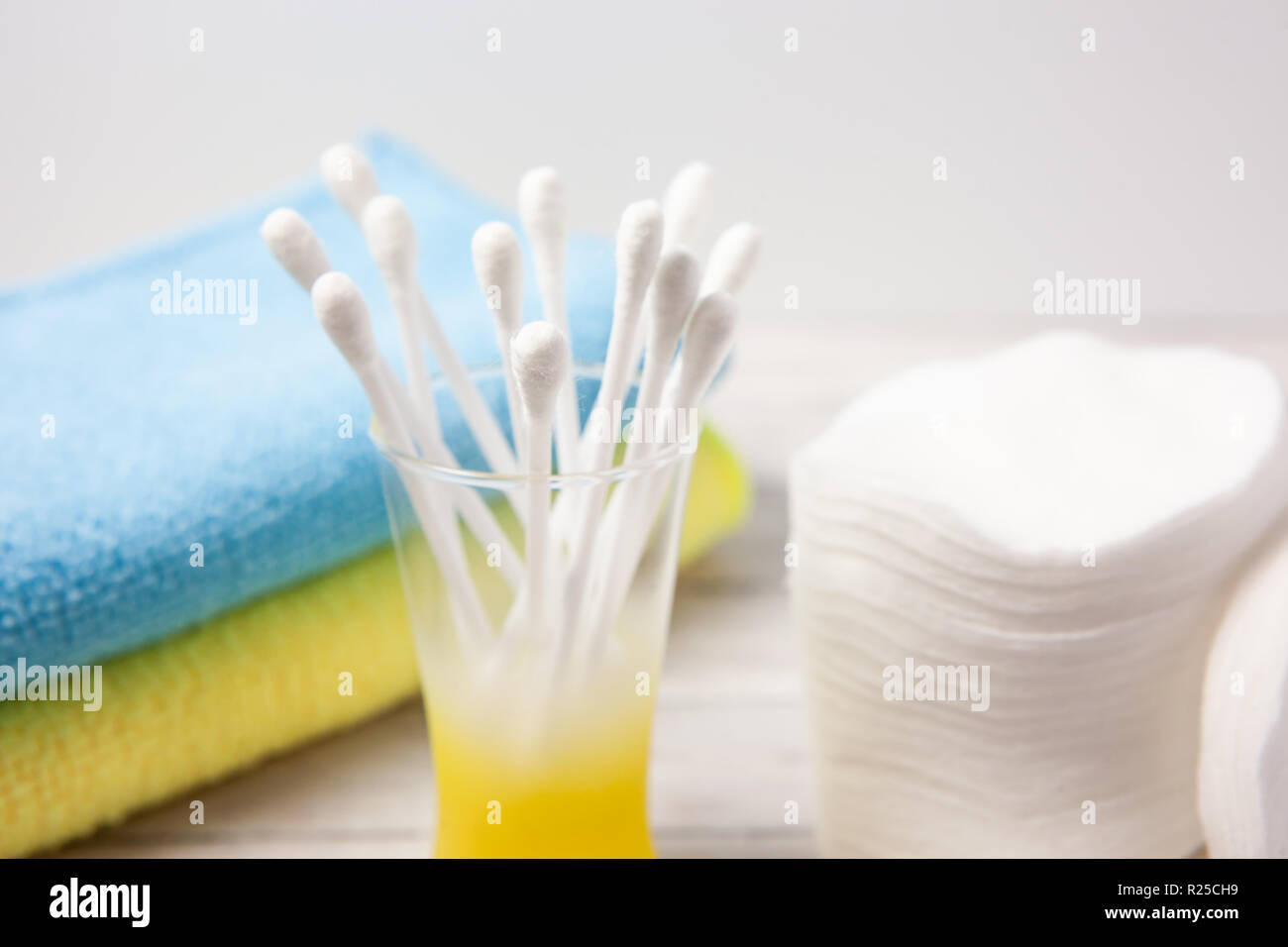 Wattepads und Sticks in einem Glas auf einen hellen Hintergrund, neben einem blauen und gelben Handtuch, das Konzept von Körper und Gesicht. Close-up Stockfoto