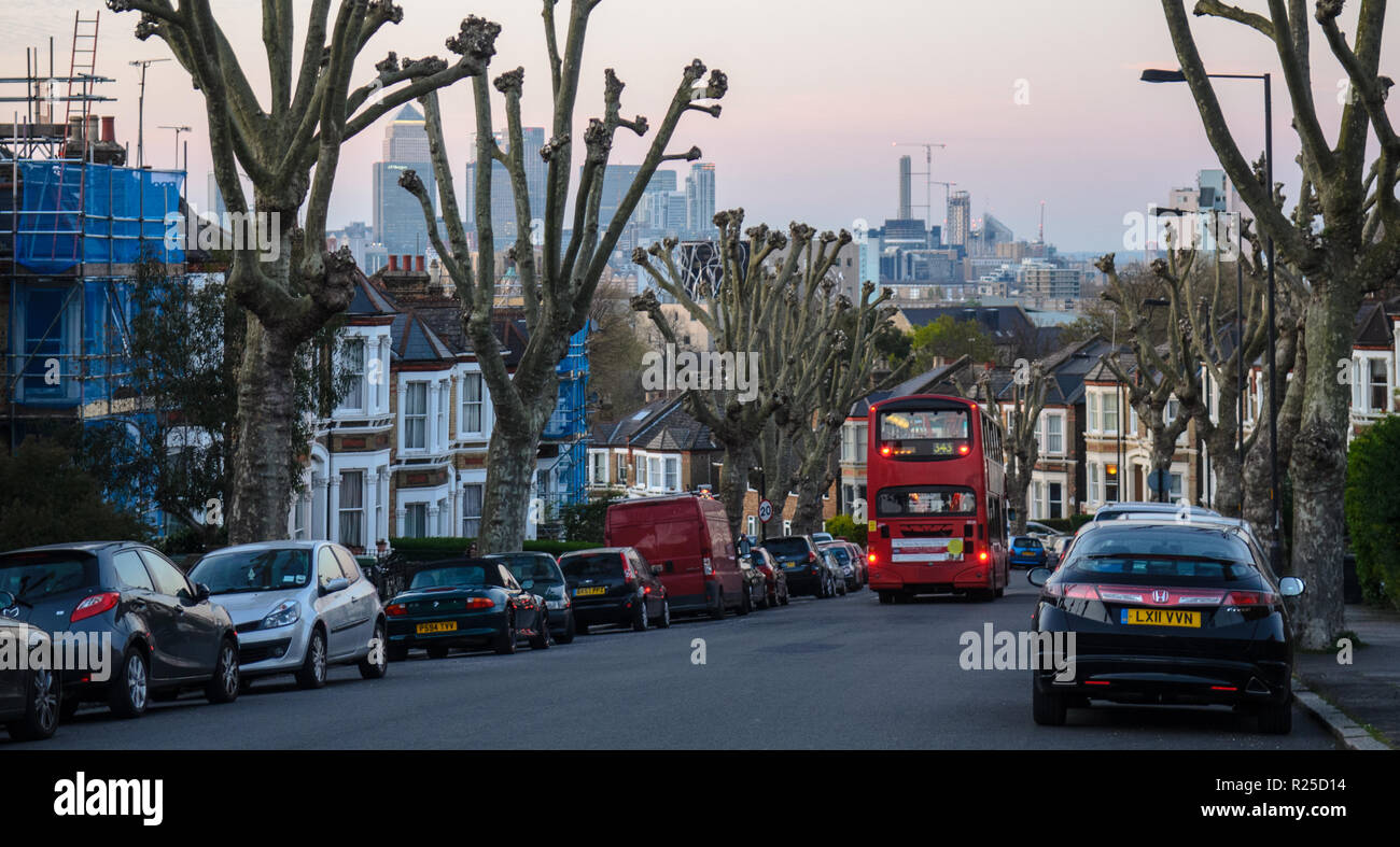 London, England, Großbritannien - 20 April 2015: Die Docklands skyline steigt hinter der traditionellen suburban Reihenhäuser und Verkehr auf einem Hügel Straße zwischen Stockfoto