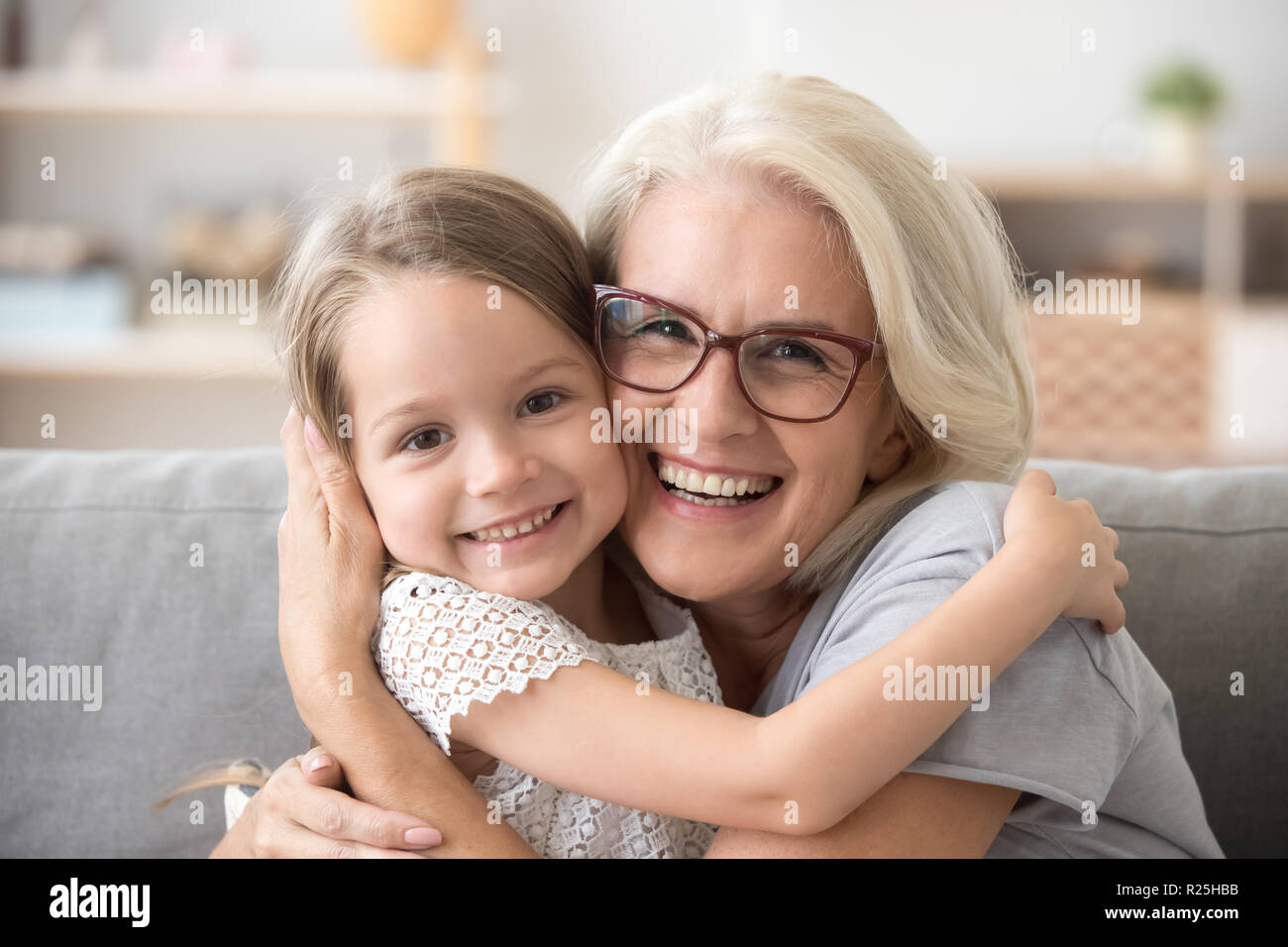 Gerne ältere Großmutter umarmt kleines Enkelkind Mädchen auf der Suche nach einem Stockfoto