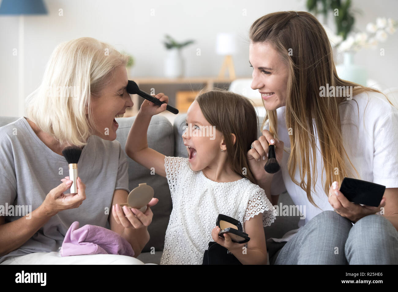 Aufgeregt Enkelin setzt Puder auf grandma tun Make-up mit Stockfoto