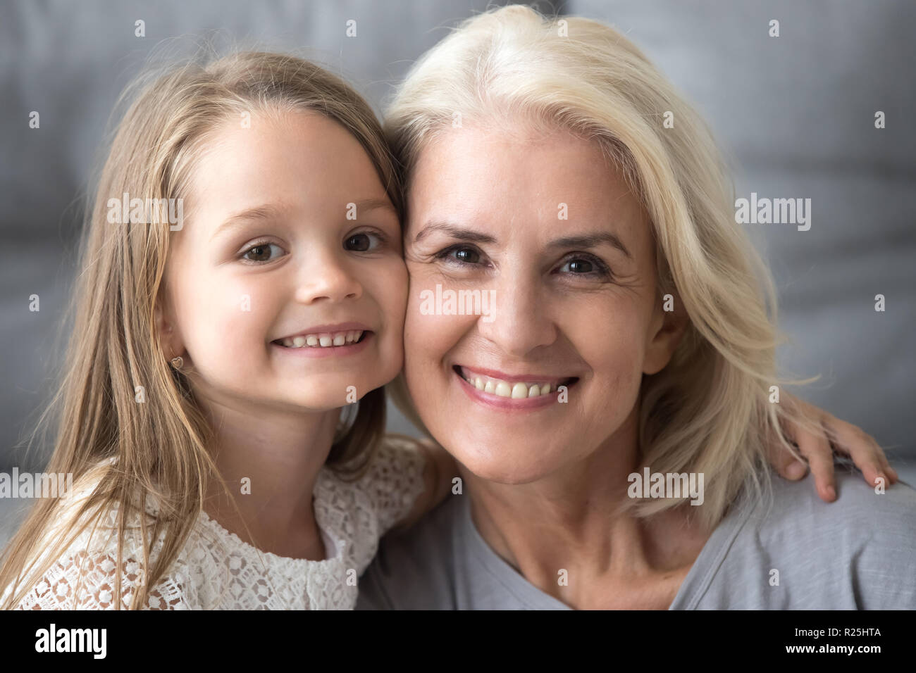 Gerne alte Großmutter umarmt lächelnden Enkelkindes auf der Suche kam Stockfoto
