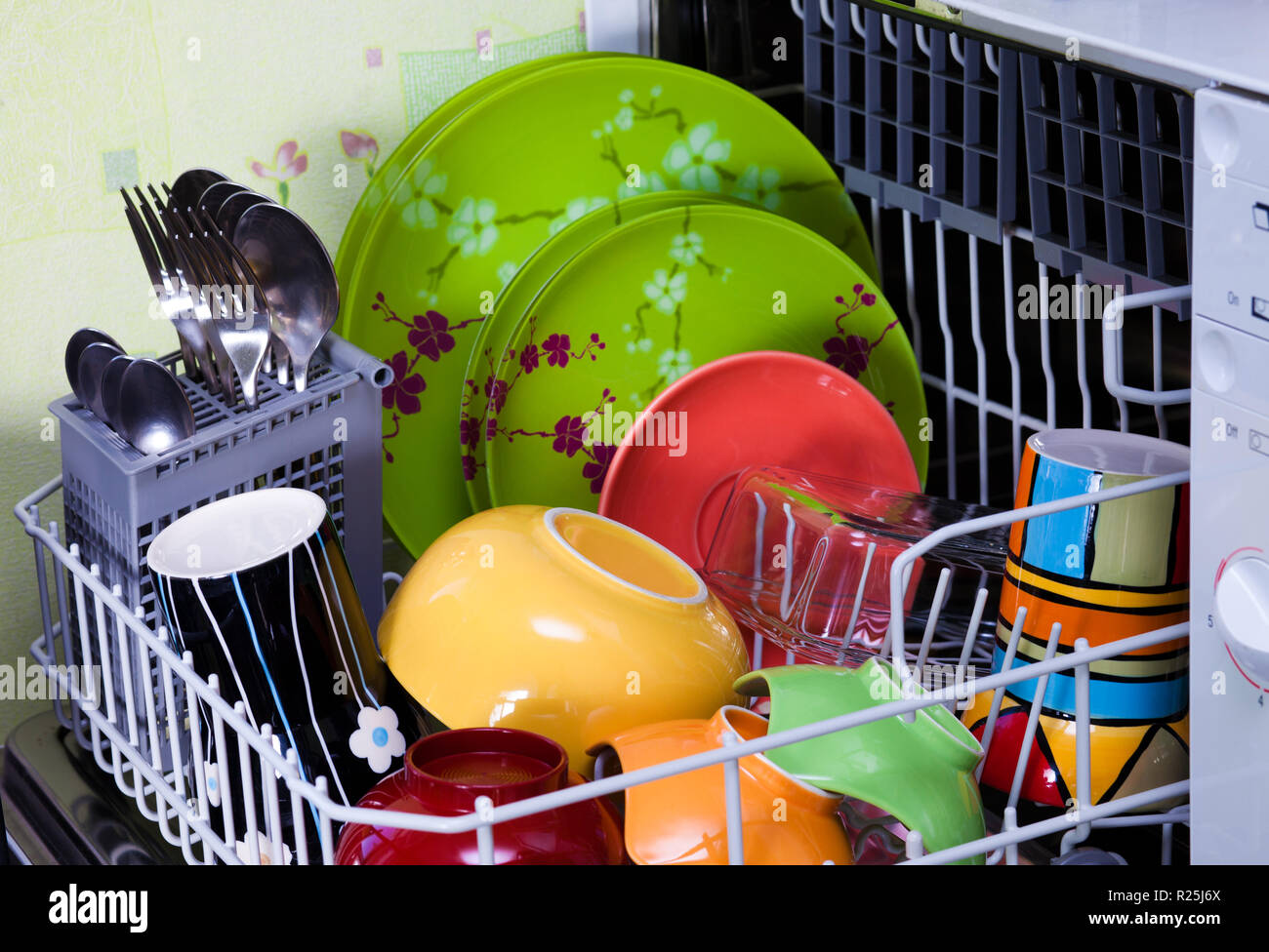 Reinigen Sie bunte Teller, Gabeln und Löffel in der Spülmaschine Stockfoto