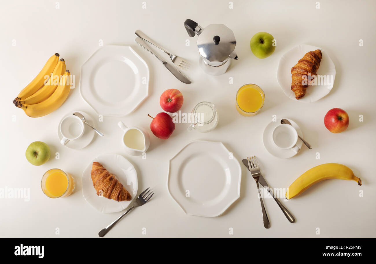 Zeit für das Frühstück. Orangensaft und Croissants, Marmelade und Honig. Kaffee mit Sahne oder Milch. Früchte wie Bananen, rote und grüne Äpfel. Frühstück auf einem weißen t Stockfoto