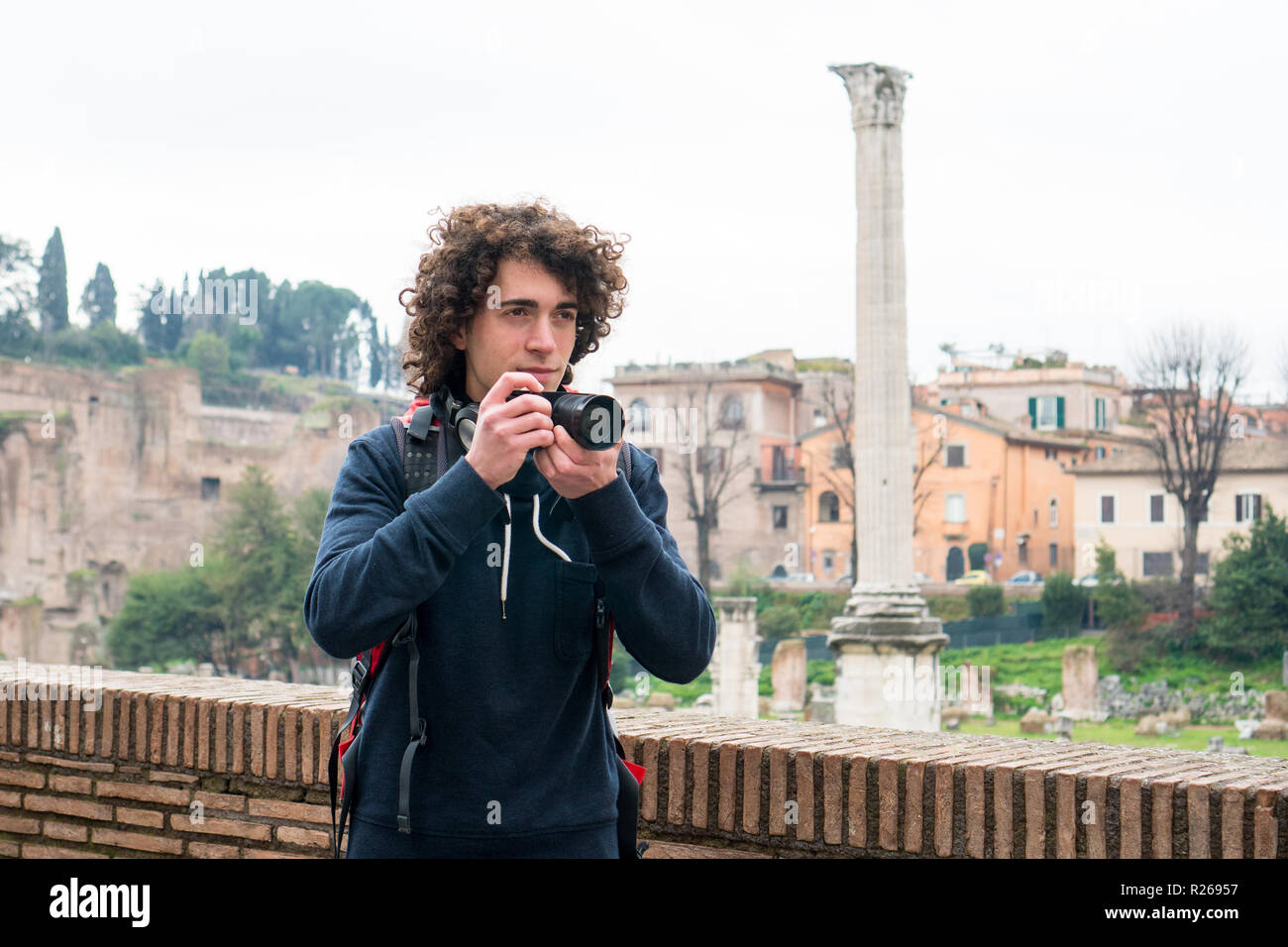 Hübscher junger Tourist mit lockigem Haar Fotos von Forum Romanum in Rom, Italien. Junger Mann mit seiner Kamera Stockfoto