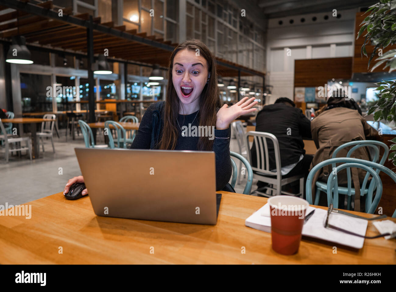 Junge, hübsche Mädchen arbeiten mit Laptop und trinken Kaffee an einem Holztisch Stockfoto