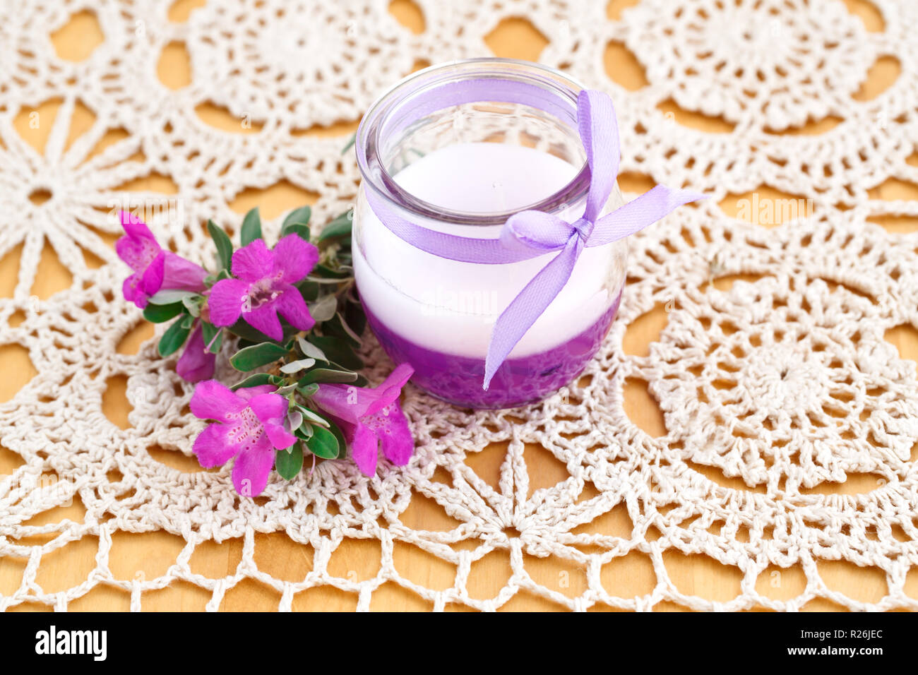 Schöne Kerze und rosa Blumen auf Hintergrund Tuch. Stockfoto