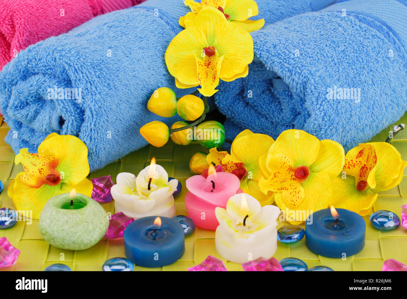 Bad mit Handtüchern, Kerzen, Steinen und Blumen auf Bambus Hintergrund gesetzt. Stockfoto
