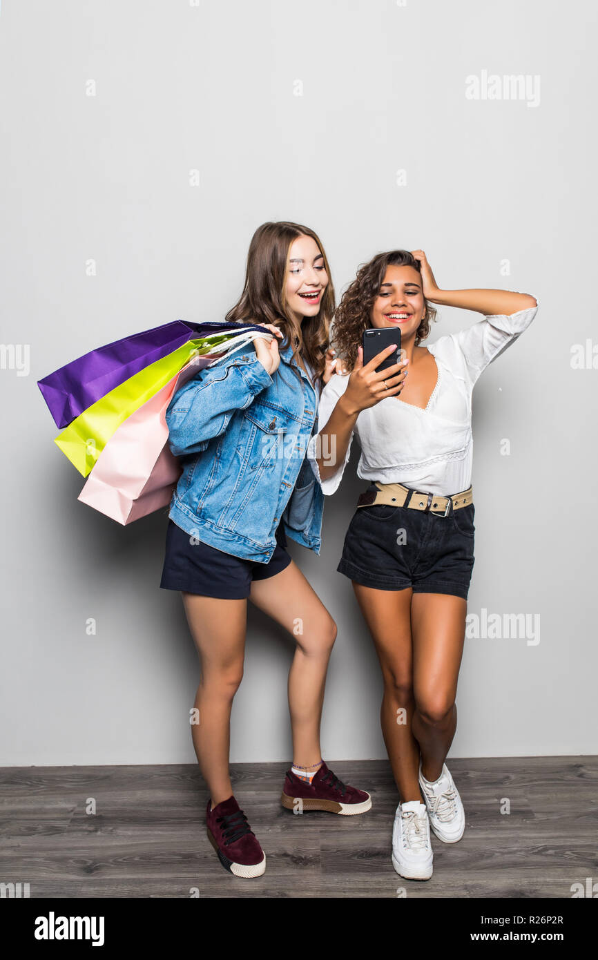 Bild der glückliche junge zwei Damen Freunde mit hellen Make-up Lippen über graue Wand stehend und mit Tüten mit Handy posieren. Suchen asid Stockfoto