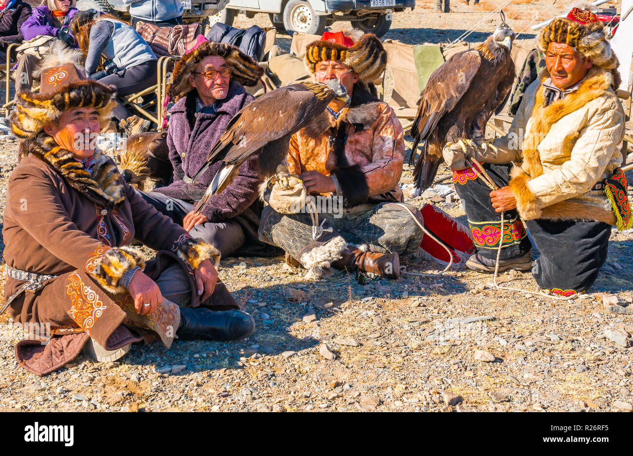 ULGII, Mongolei - OKTOBER 6, 2018: Golden Eagle Festival. Kasachischen eagle Jäger in traditioneller Kleidung saß auf dem Boden warten, um den Wettbewerb in Ul Stockfoto