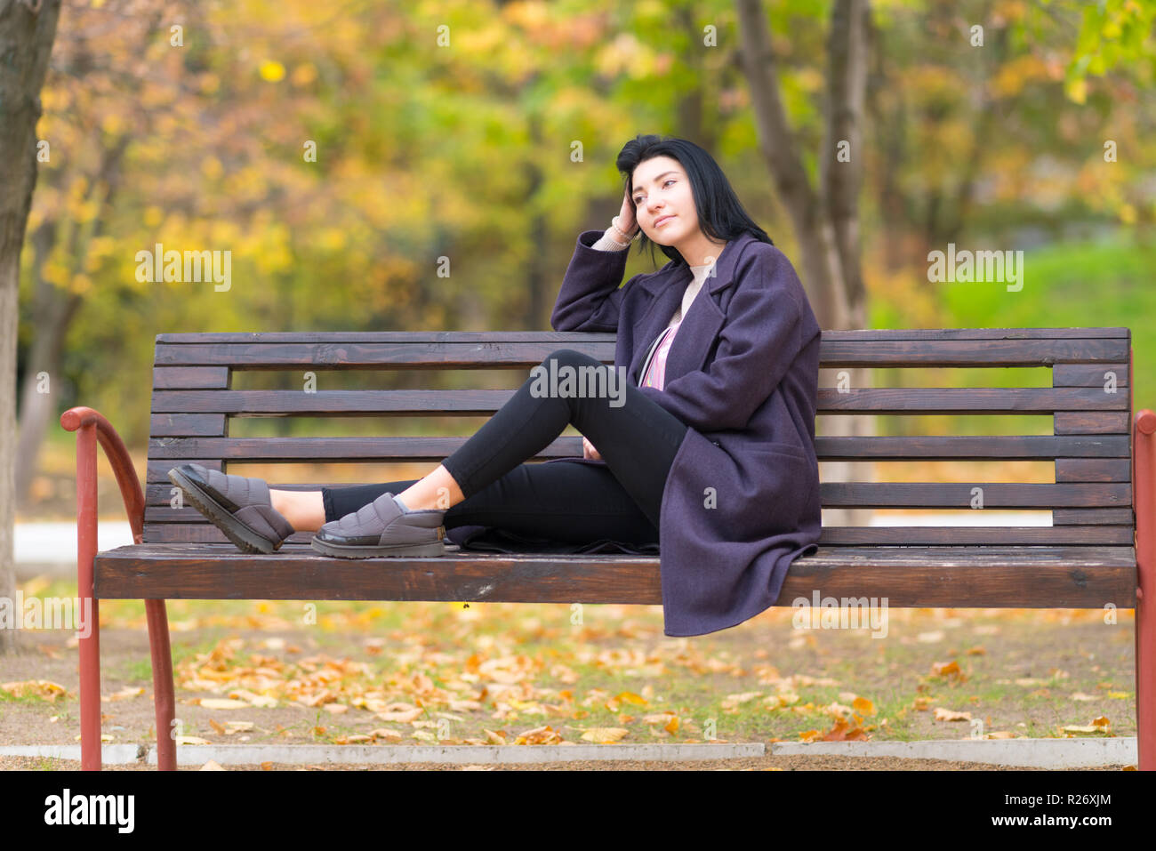 Junge Frau in einem Park denken Tief mit ihren Füßen saß auf einem urigen Holzbank starrte auf die Seite Stockfoto