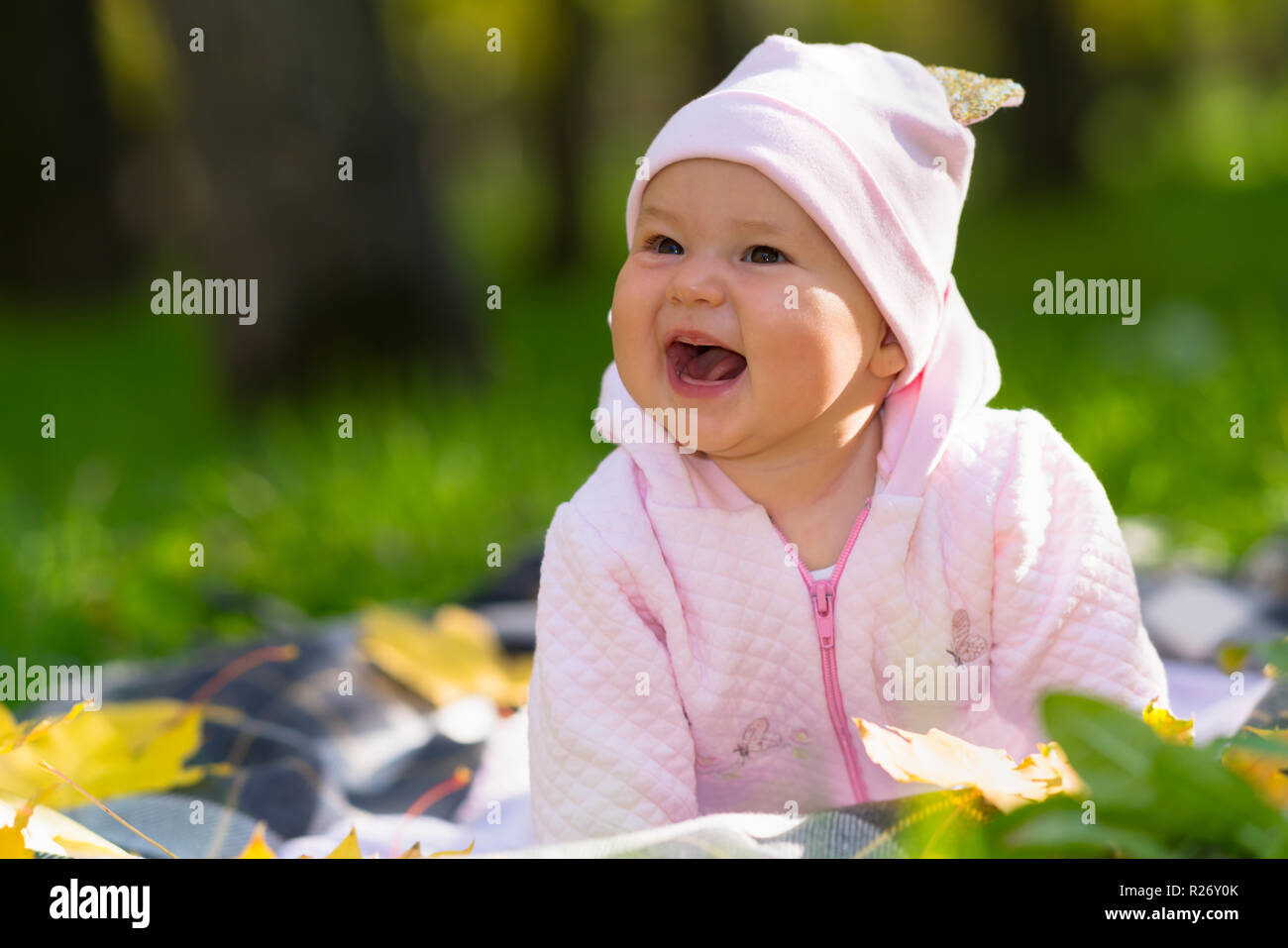 Lachendes Baby Mädchen mit einem breit strahlenden Lächeln spielen auf einer Decke auf dem Rasen in einem Herbst Park in eine ehrliche Portrait Stockfoto