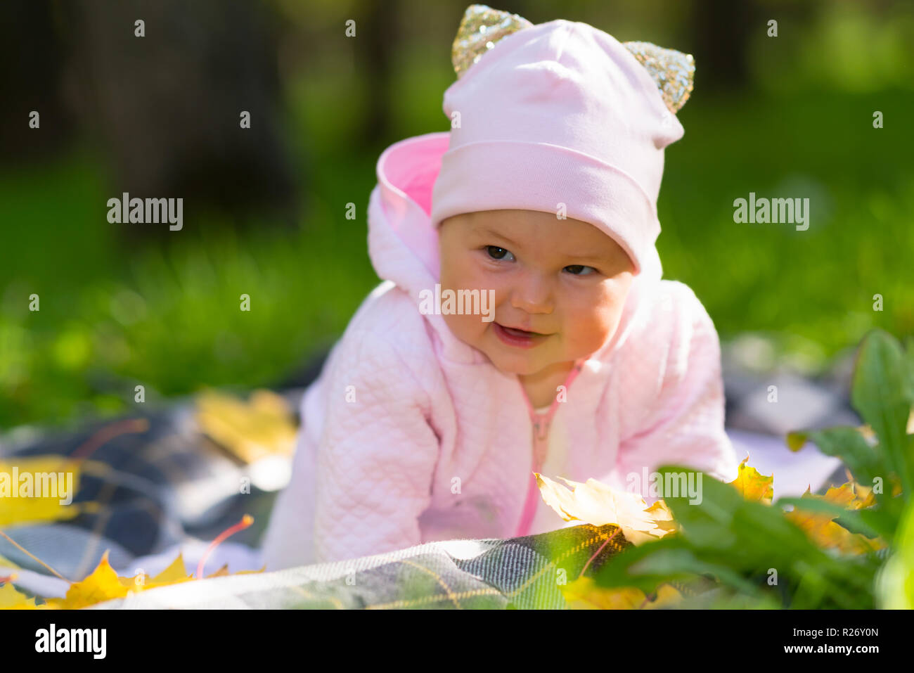 Recht fröhliche kleine Baby Mädchen in einem Herbst Park auf ihre Decke im Gras auf die Kamera mit einem glücklichen Lächeln Stockfoto
