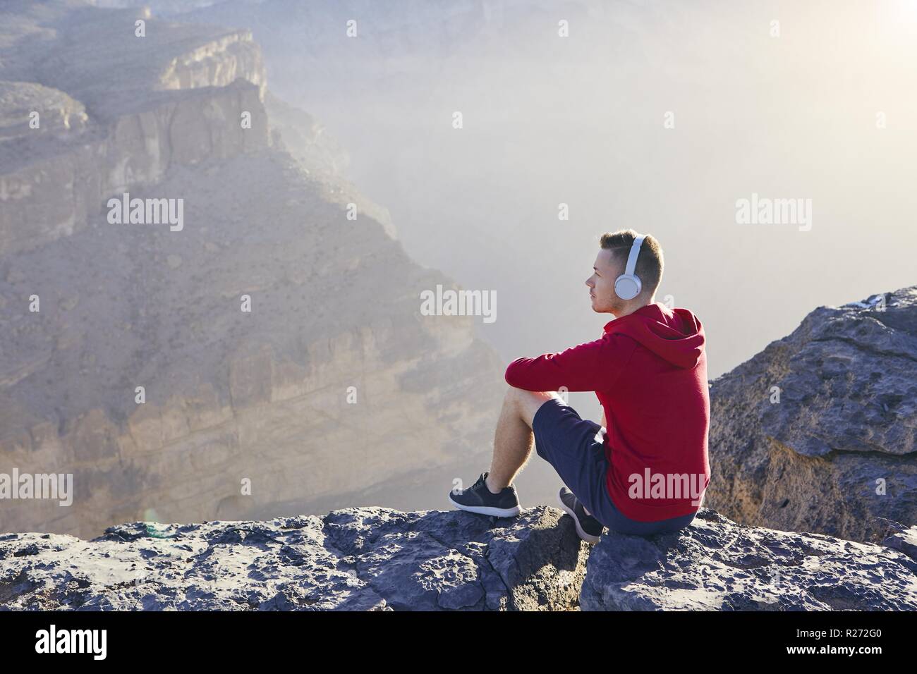 Entspannung in den Bergen. Junger Mann mit Kopfhörer sitzen auf den Rand der Klippe und hören Musik. Stockfoto
