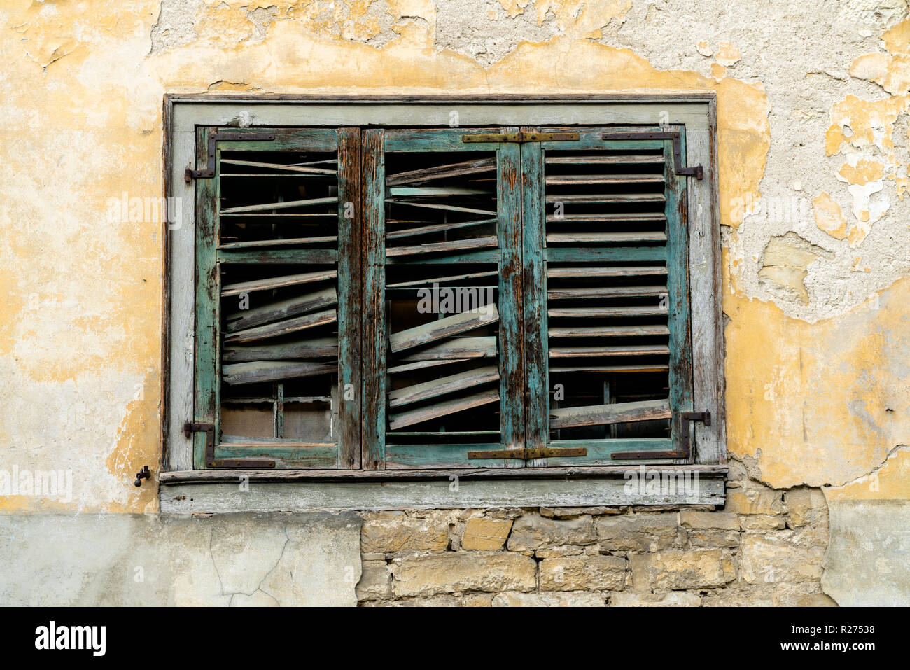 Alte kaputte Fenster Fensterläden auf einem Verfallenen und heruntergekommen Haus front mit abgeplatzte Farbe und Gips Stockfoto