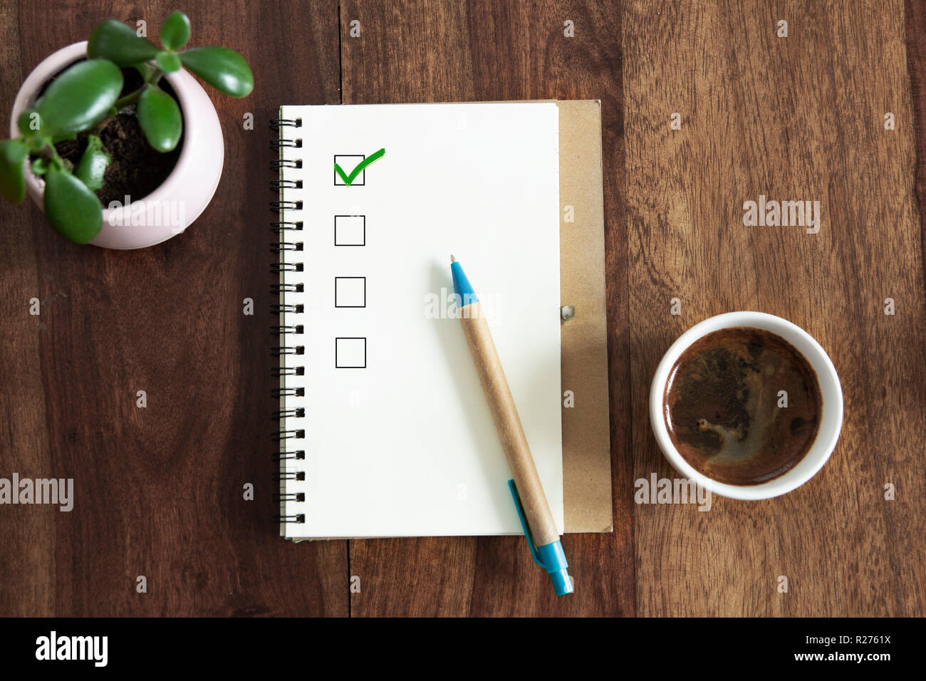 Aktivieren Sie das Kontrollkästchen in Notepad auf Tisch. nach oben Blick auf hölzernen Tisch mit leeren Notizblock, Stift und die Tasse Kaffee. Stockfoto