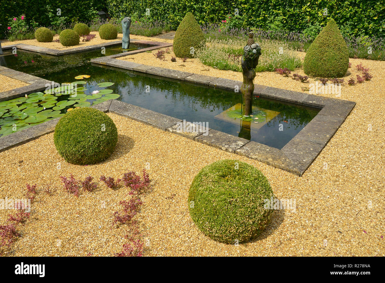 Wasserspiel IN EINEM LAND HAUS GARTEN. AUGUST 2018. OAKHAM, Rutland, England. Eine decortive formale Wassergarten mit Formschnitten und Statuen Stockfoto
