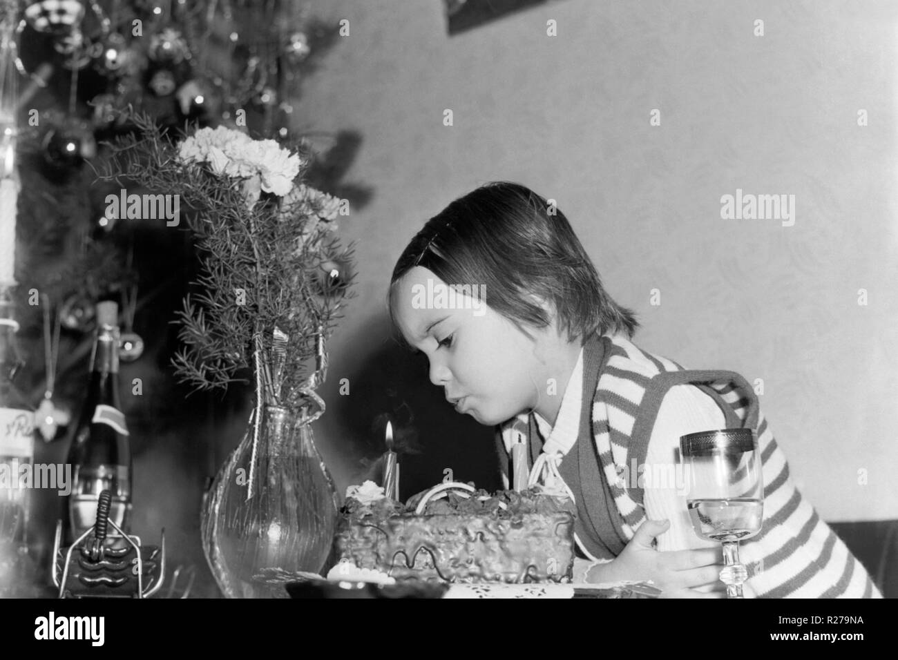 Junge Mädchen bläst die Kerzen auf der Torte mit Weihnachtsbaum im Hintergrund 1970 s Ungarn Stockfoto