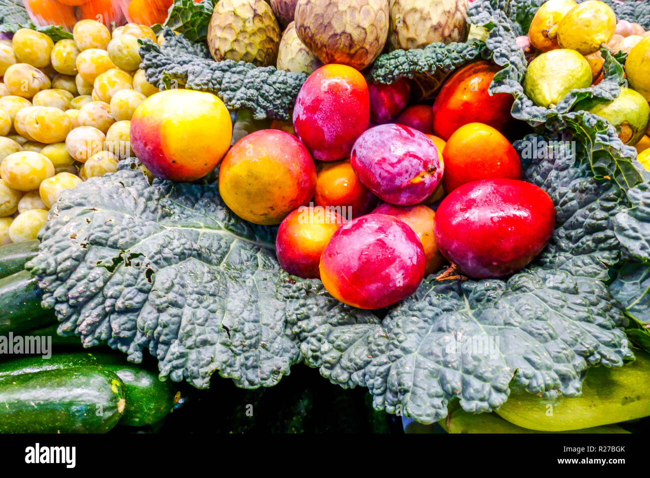 Frische rote Mangos und gelbe Pflaumen auf savoyenkohlblättern auf einem Bauernmarkt in Valencia, Spanien. Stockfoto