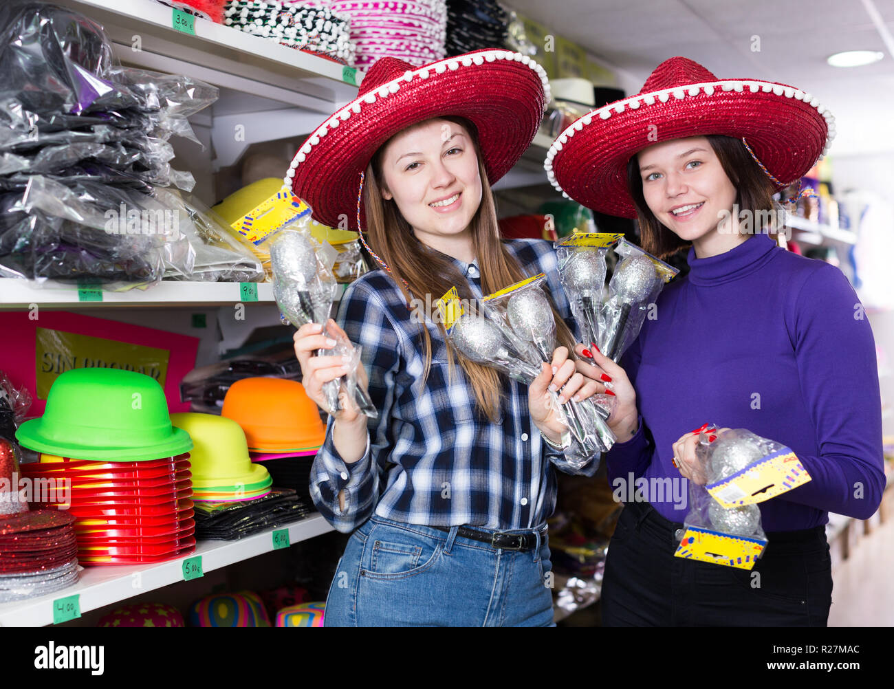 Porträt von zwei fröhliche Mädchen in den Sombrero mit Maracas in Händen während der Vorbereitung für die Partei in festlichem Sachen shop Stockfoto