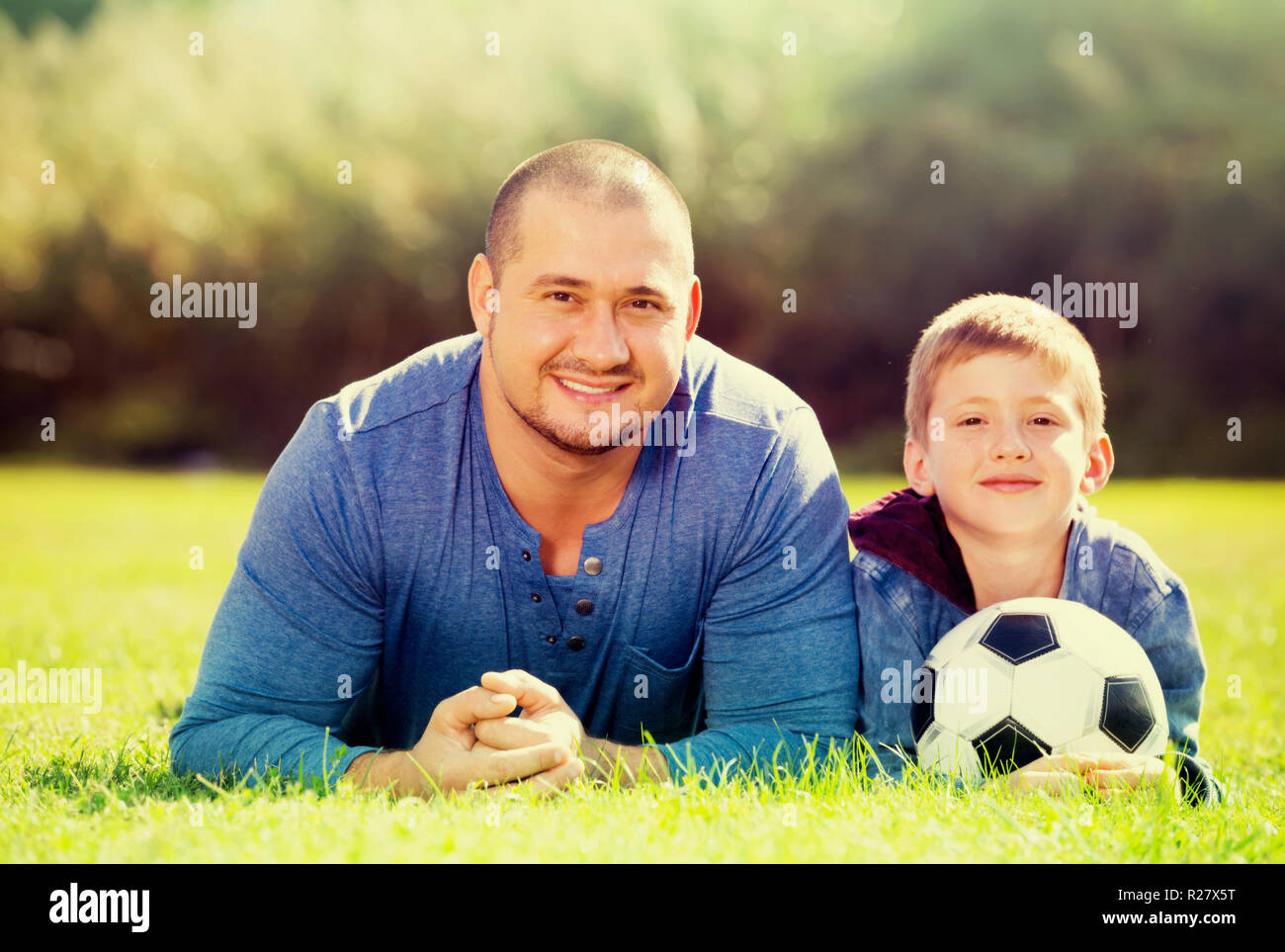 Freundlich lächelnden Teenager Sohn und Vater im Gras liegend zusammen mit Fußball-Ball. Fokus auf den Menschen Stockfoto