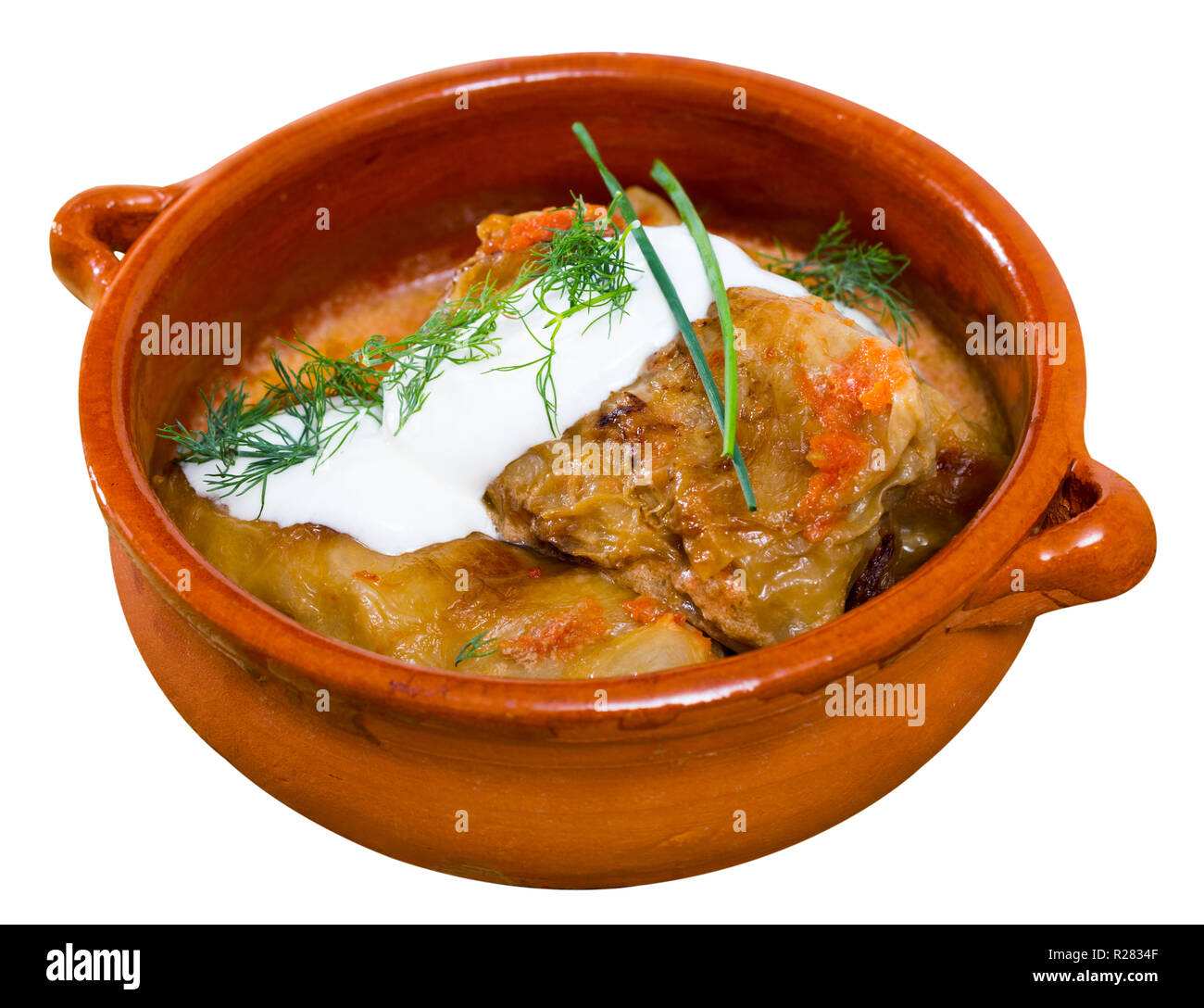 Leckere Kohlrouladen in Blättern von Kohl in Tontopf mit Sauerrahm und Grüns. Auf weissem Hintergrund Stockfoto