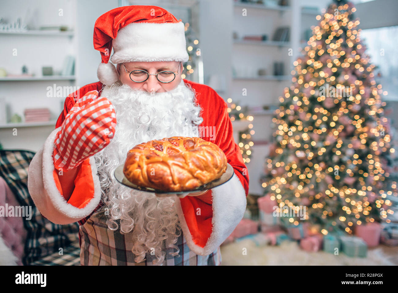 Frisch und lecker Torte ist in den Händen von Santa Claus. Er sieht und riecht. Es gibt Weihnachten Baum hinter ihm. Stockfoto
