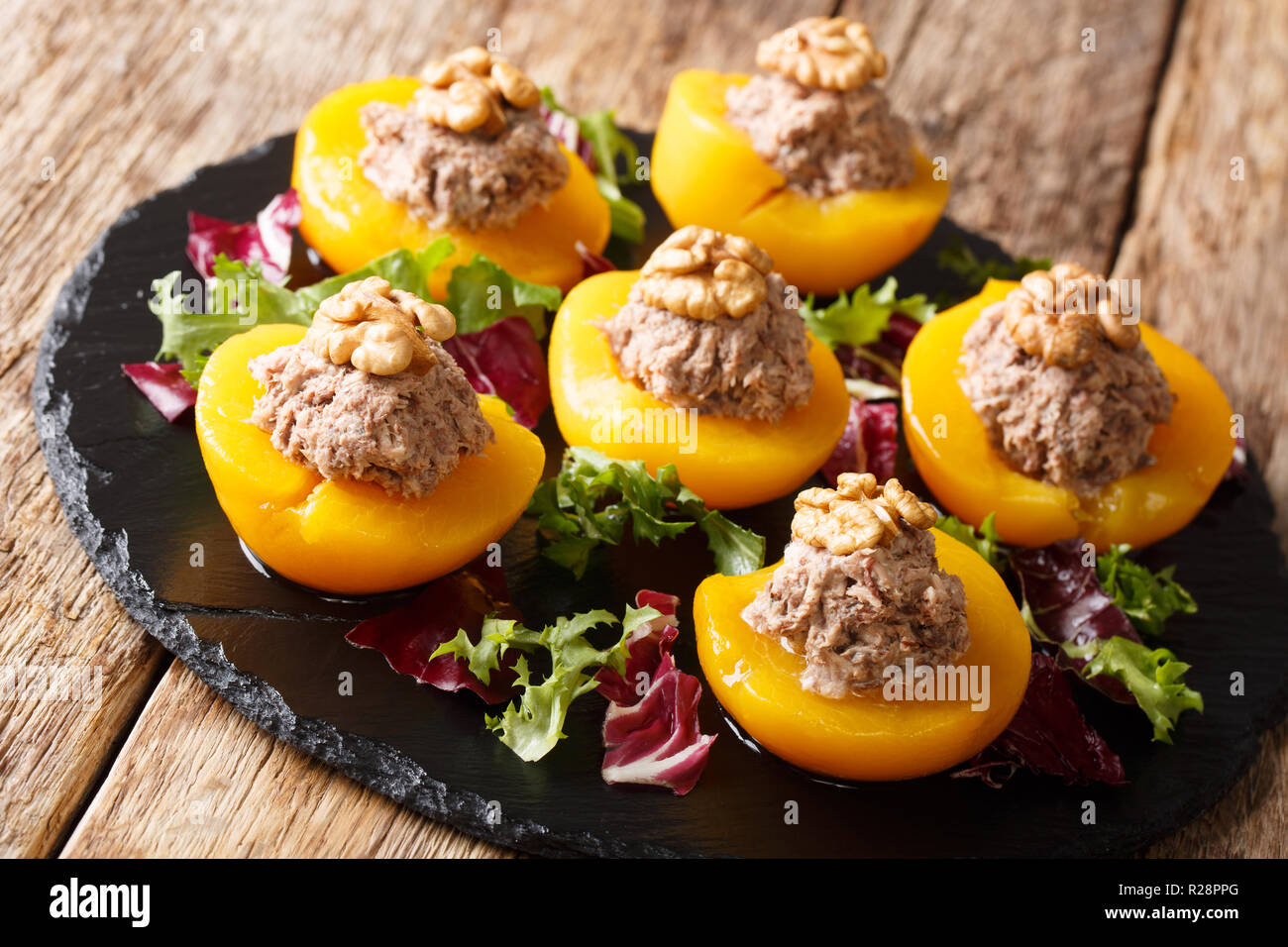 Festliche Vorspeise von Pfirsichen, gefüllt mit Thunfisch Mousse und Walnüsse, serviert mit Blattsalat close-up auf dem Tisch. Horizontale Stockfoto