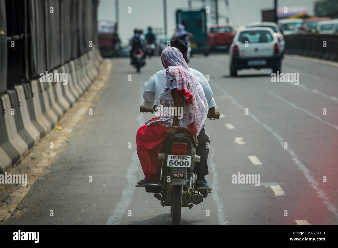 Eine Frau reitet Sozius auf einem Motorrad auf einer Straße in New Delhi, Indien. Stockfoto