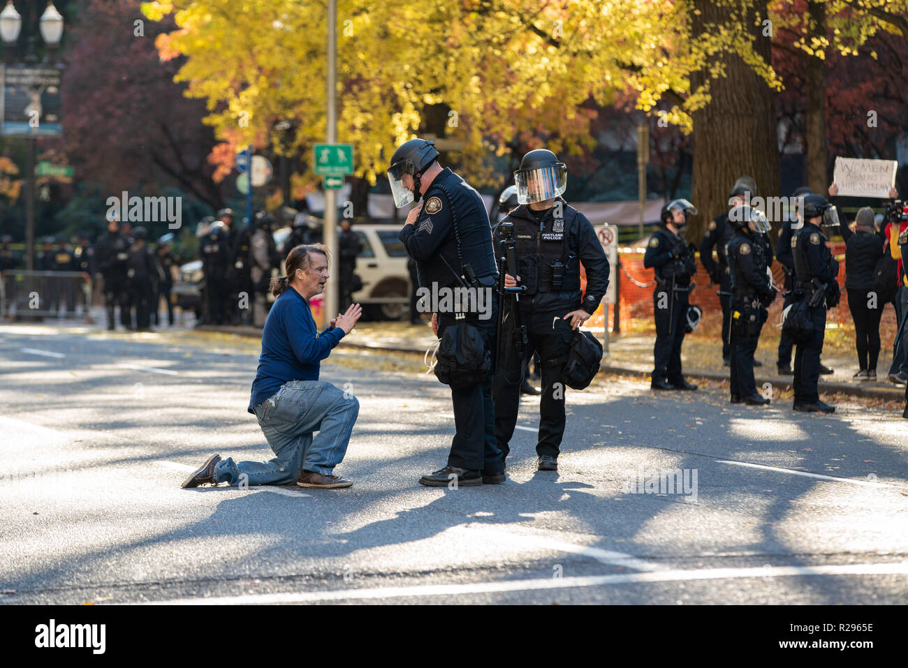 Portland, OR/USA, 17. November 2018: Demonstrator in der Innenstadt von Portland auf seinen Knien in der Mitte der Straße. Zwei Polizisten versuchen, Grund Stockfoto