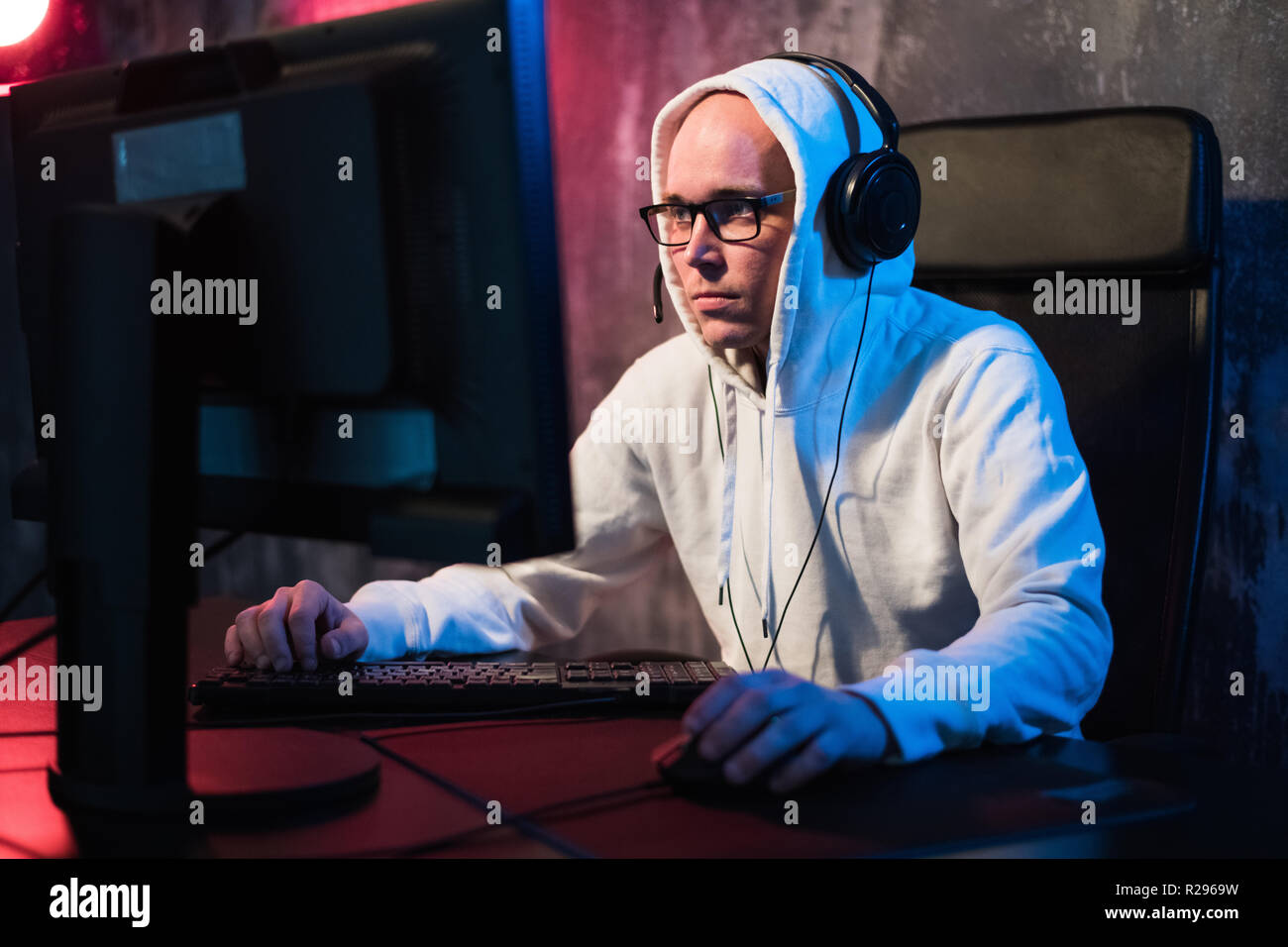 Portrait von konzentrierter junger Mann in Gläsern und Headset in den dunklen Raum spielen online computer spiel oder konkurrierenden im online-esport Turnier. Stockfoto