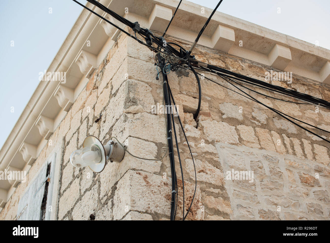 Elektrische Leitungen auf einem alten Haus aus Stein angebracht. Alte Architektur. Stromübertragung. Die Glühbirne auf dem Gebäude. Street Light. Stockfoto