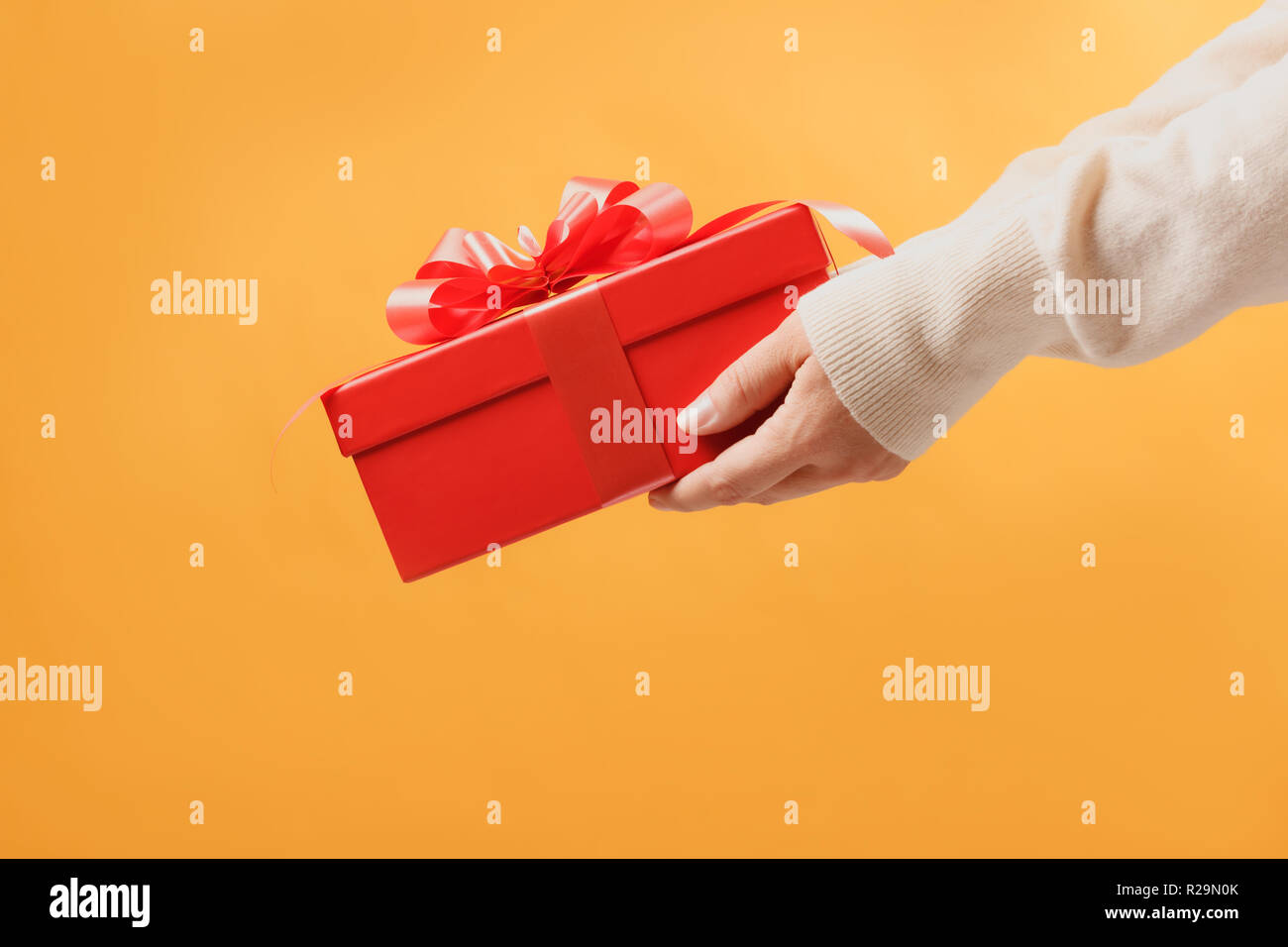 Close-up Teilansicht der Mann in der Strickjacke mit roten Geschenkkarton auf gelben Hintergrund. Geschenk, das Konzept. Stockfoto