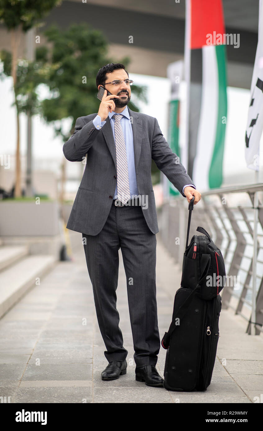 Arabische Geschäftsmann mit seinem Koffer in einer Stadt, die auf einem Telefon Stockfoto