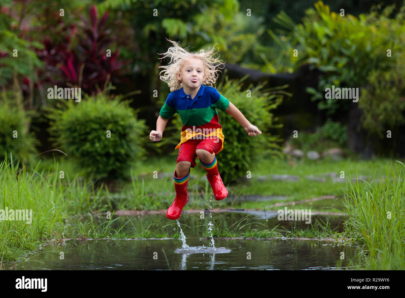 Kid spielen im Regen stehen. Kinder mit Schirm und regen Türkis Blaue Stiefel Auf Mädchen Spielen Im Wasser Pfütze