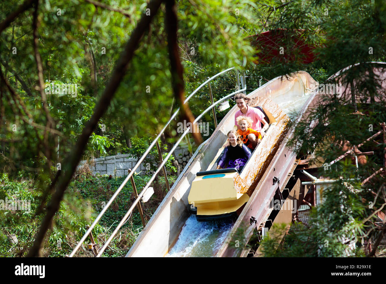 Familie mit Kindern auf der Achterbahn im Freizeitpark Theme Park. Kinder, die auf hohe Geschwindigkeit Rutsche Attraktion in der Unterhaltung Kirmes im Sommer Stockfoto