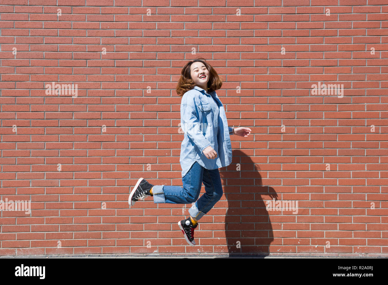 Schönen lächelnden jungen Frau in einer glücklichen Sprung mit Rote Wand Hintergrund Stockfoto