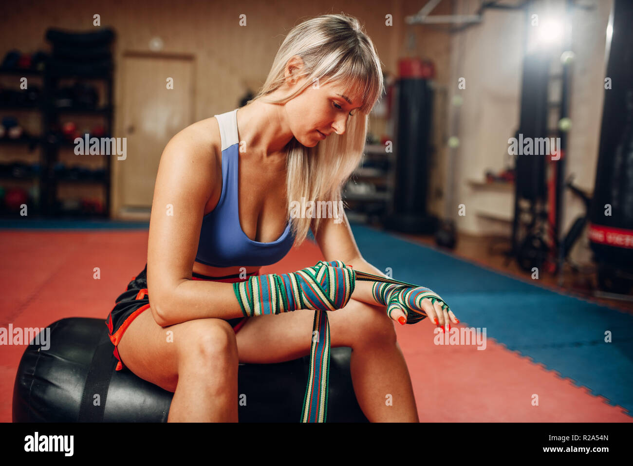 Weibliche kickboxer im Boxen Bandagen und Sportswear sitzen auf Boxsack nach dem Training im Fitnessraum. Frau Boxer auf Training, Kickboxen Praxis Stockfoto