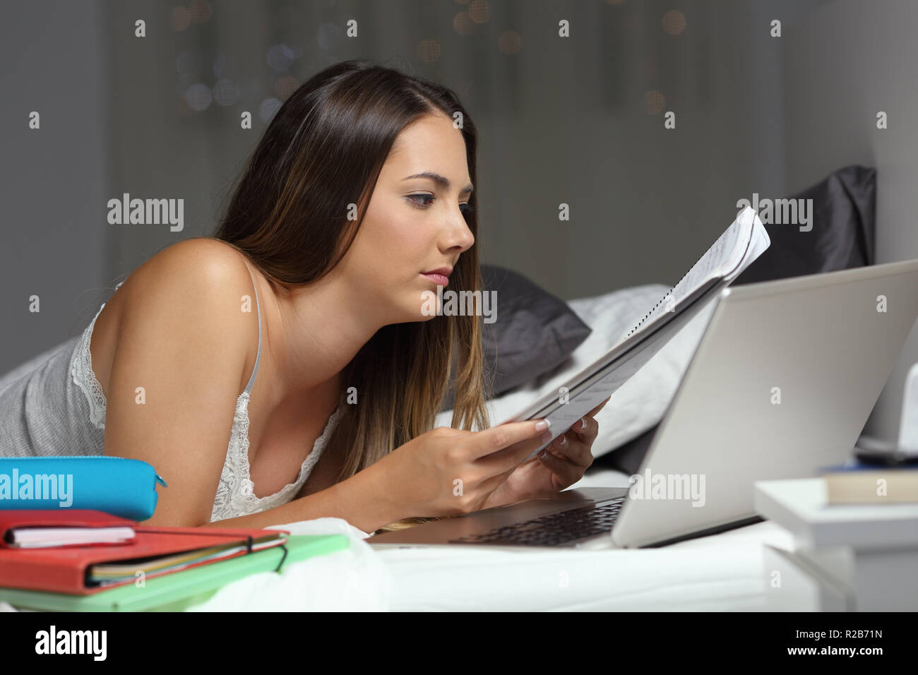 Studious student Studium der späten Stunden Vergleich der Notizen auf dem Bett in der Nacht zu Hause liegen Stockfoto