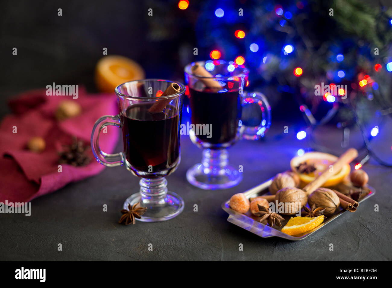 Winter Zusammensetzung. Rote Glühwein in Gläsern auf schwarzen Hintergrund. Tanne Kranz, elektrische Lampen, Fach mit Orange, Zimt, Nüssen und Gewürzen, rot n Stockfoto
