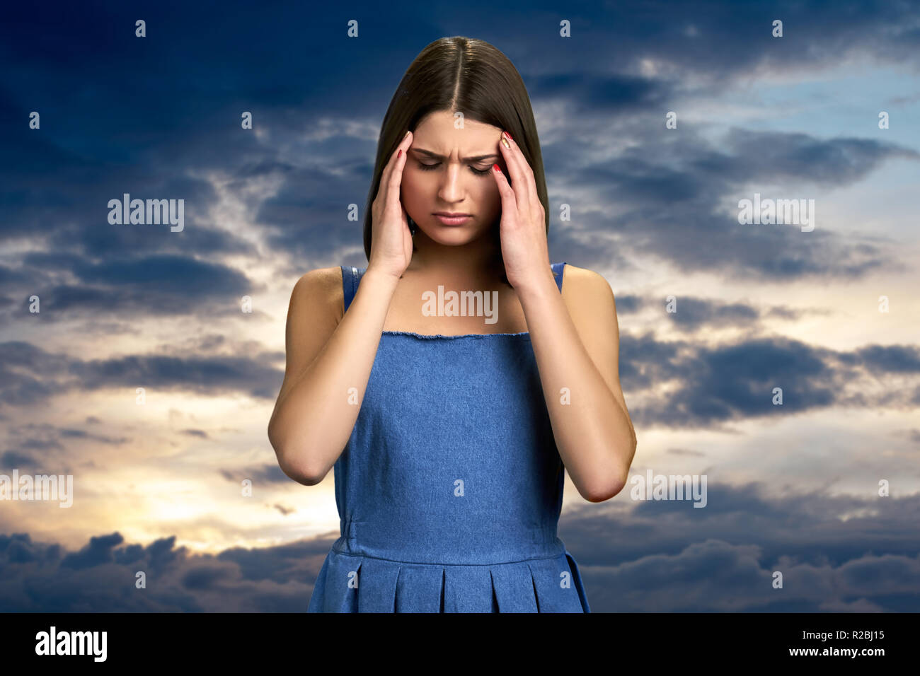 Kaukasische Frau mit schrecklichen Migräne. Schöne umgekippt Mädchen leiden unter Kopfschmerzen am Abend Himmel Hintergrund. Menschliche Ausdrucksformen der Schmerz. Stockfoto