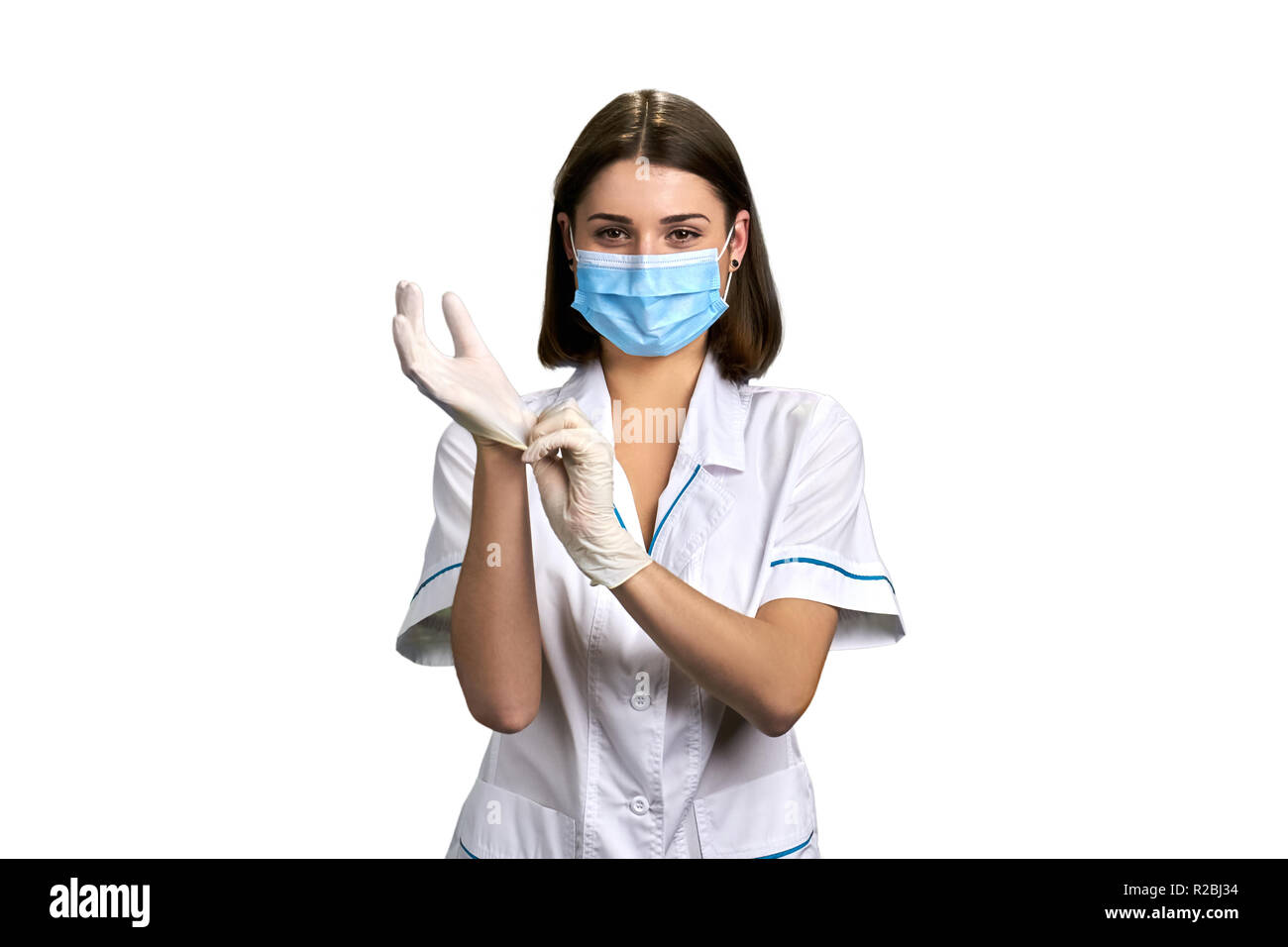 Weibliche attraktive Arzt setzt auf Handschuhe. Ziemlich Facharzt mit medizinischen Maske und weiß Latex Handschuhe auf weißem Hintergrund. Stockfoto