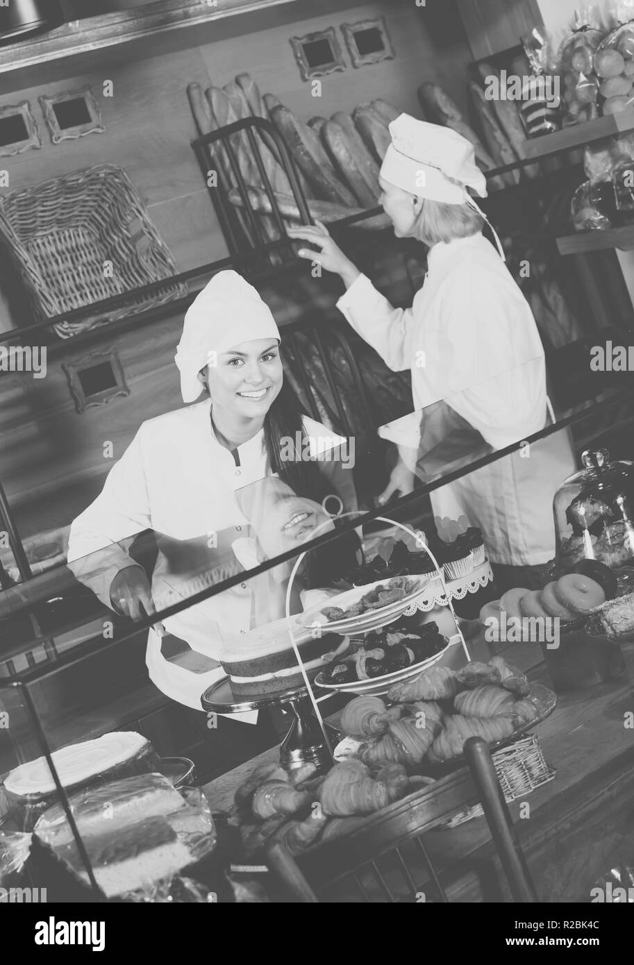Positive junge Frau und reife Assistant bietet fancy und Schwamm Kuchen für den Verkauf in Kaffee - Haus Stockfoto