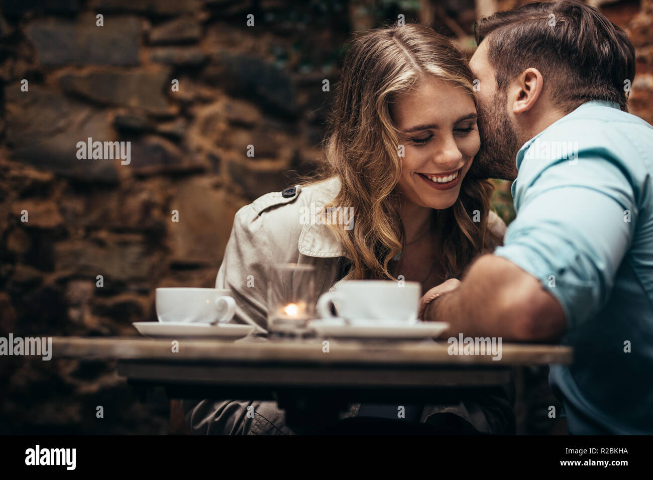 Glückliches Paar sitzen zusammen in einem Café mit Tassen Kaffee auf Tisch. Romantisches Paar auf ein Date mit dem Mann küsste seine Freundin. Stockfoto