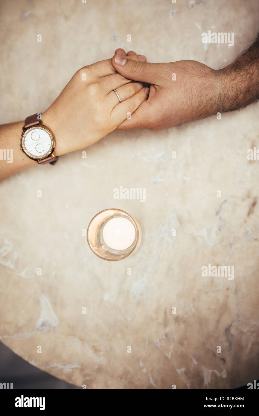 Blick von oben auf die Hände von Mann und Frau einander halten. Romantisches Paar Hand in Hand auf einen Tisch mit Kerze Glas von der Seite. Stockfoto