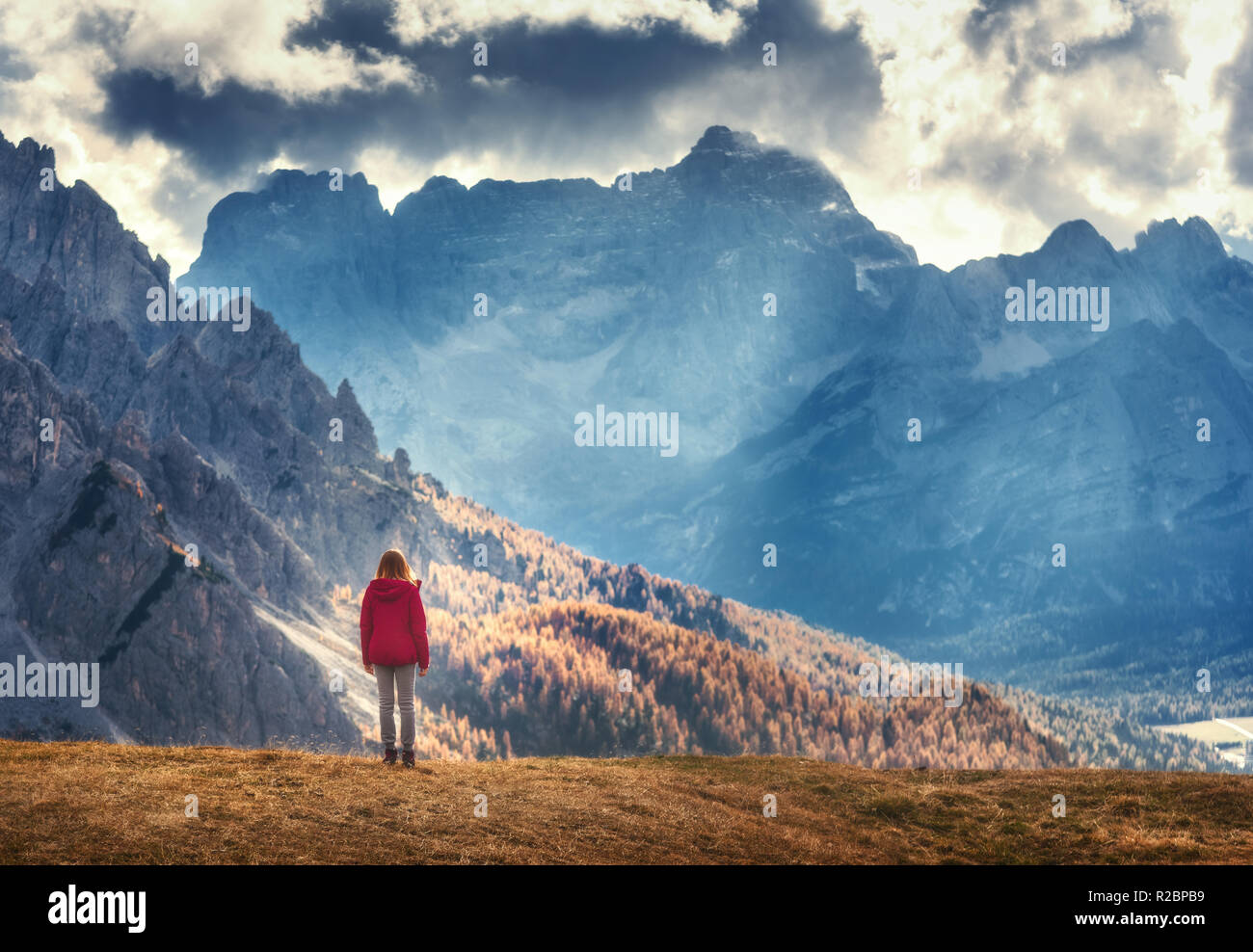 Junge Frau auf dem Hügel schaut auf die majestätischen Berge bei Sonnenuntergang im Herbst in den Dolomiten, Italien. Landschaft mit Mädchen, bewölkter Himmel, Sunbeam, hohe r Stockfoto