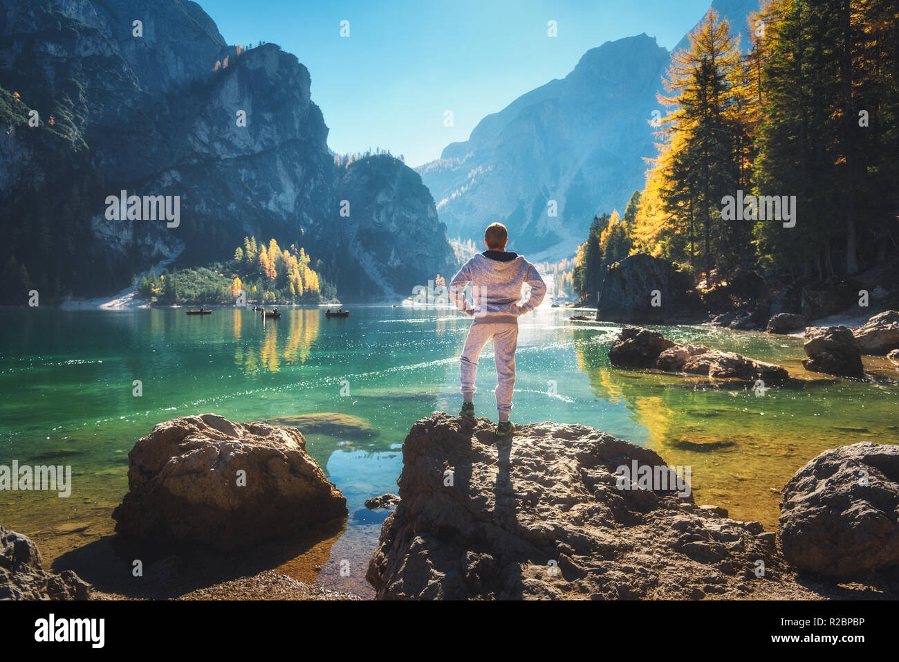 Ständige sportliche Mann auf dem Stein an der Küste von Pragser See bei Sonnenaufgang. Herbst in den Dolomiten, Italien. Landschaft mit glücklichen Menschen, Berge, Wasser mit r Stockfoto