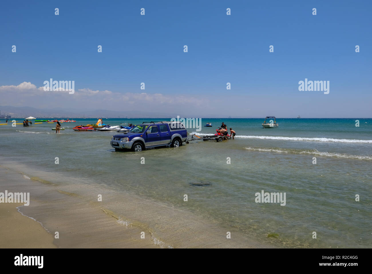 Lady's Mile, Limassol, Zypern - 23. Juni 2018: Beach Szene mit einem 4x4 Jeep im Wasser, und drei Menschen Laden eines Jet Ski. Stockfoto