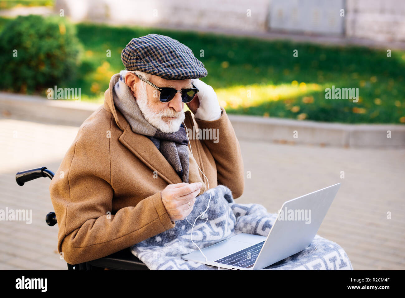 Schöne ältere behinderte Menschen im Rollstuhl mit Laptop mit Kopfhörern auf der Straße Stockfoto